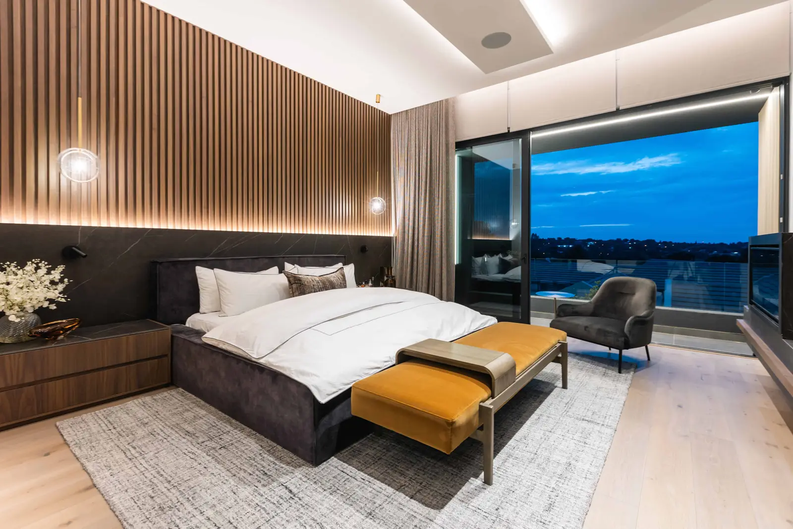 Modern bedroom with timber slat wall, warm tones, and night view over Steyn City, designed by Renovatio Interiors Johannesburg.