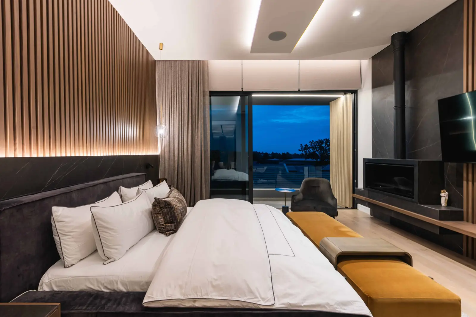 Modern bedroom with timber slat wall, warm tones, and night view over Steyn City, designed by Renovatio Interiors Johannesburg.