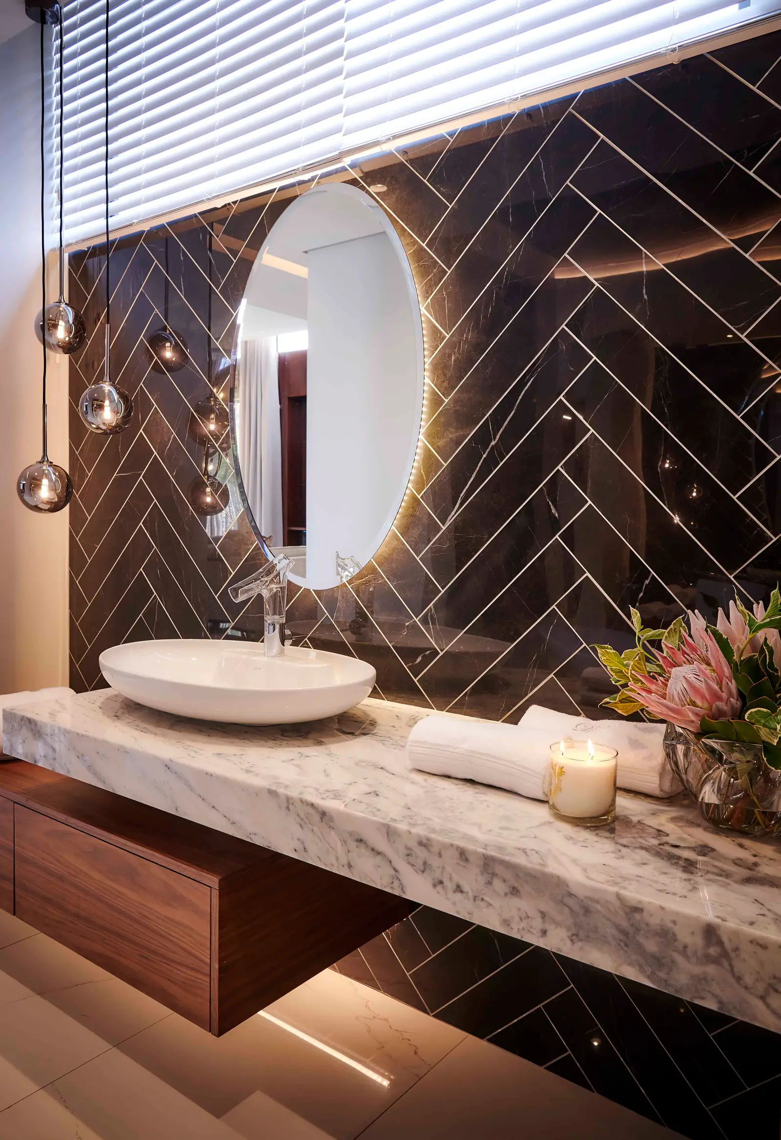 Contemporary bathroom with a round mirror, sleek vanity and herringbone tile work designed by Interior Designer Johannesburg.