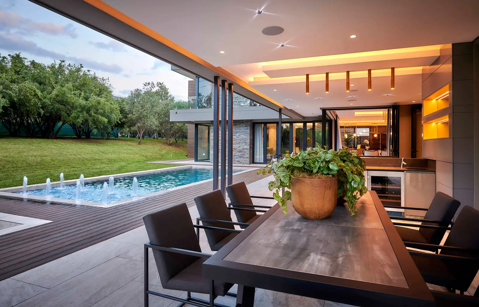 Covered patio dining space with wooden table, pendant lighting and pool view created by Interior Designer Johannesburg.