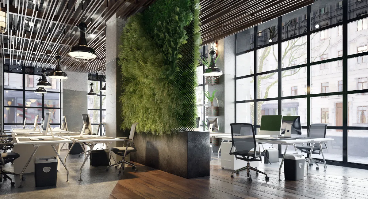 Modern commercial office interior featuring a collaborative workspace with white desks, ergonomic chairs, large industrial-style windows, and a striking vertical green wall under a wood-slat ceiling — showcasing biophilic design and natural light integration.